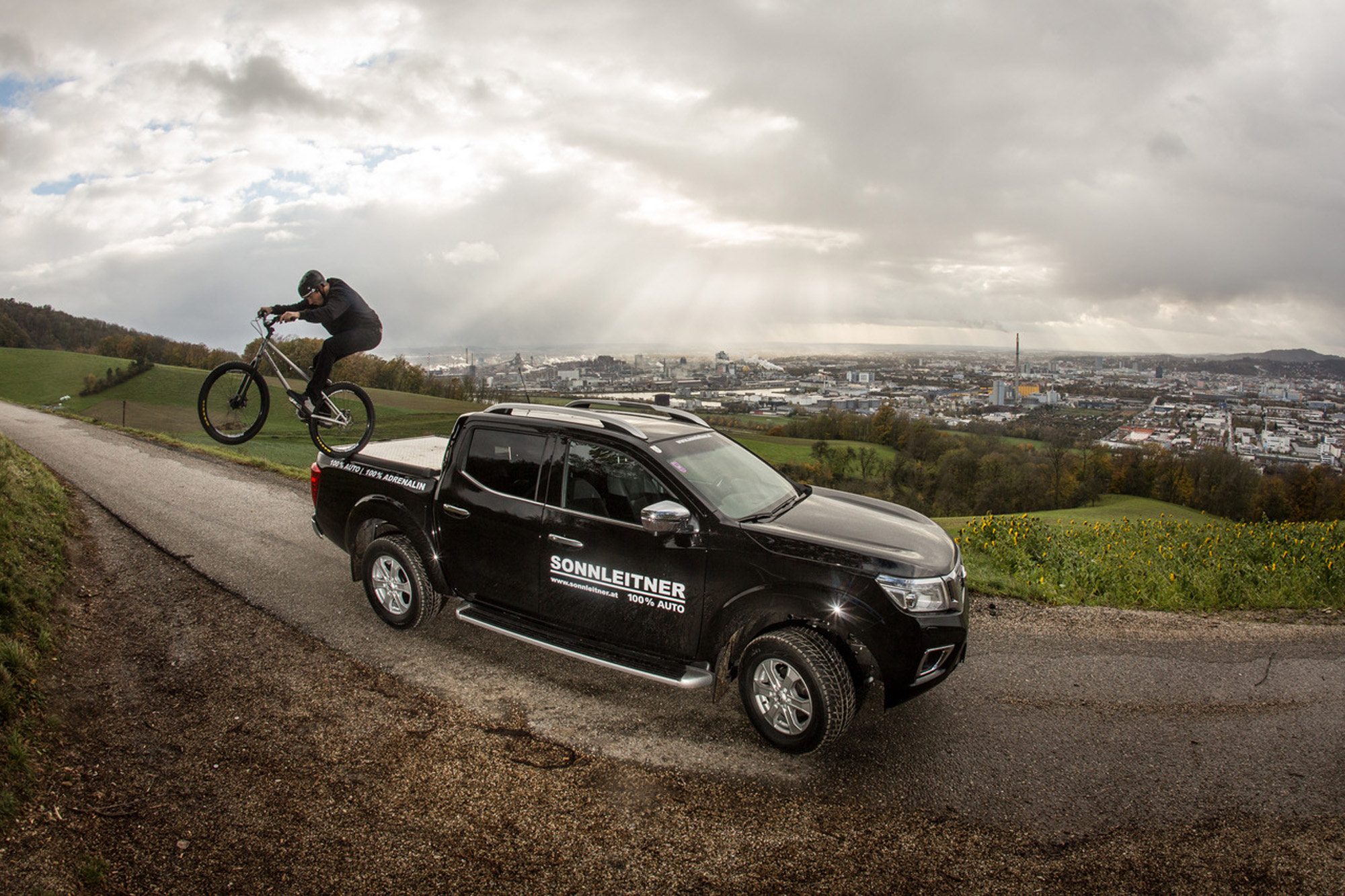 Dominik Raab bei einem Sprung von seinem Nissan Navara mit Blick über Linz