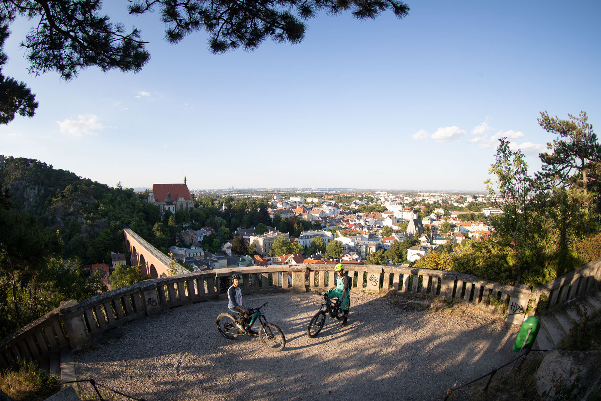 Dominik und Alban sitzen auf ihrem Bike und man sieht die Dächer Wiens im Hintergrund