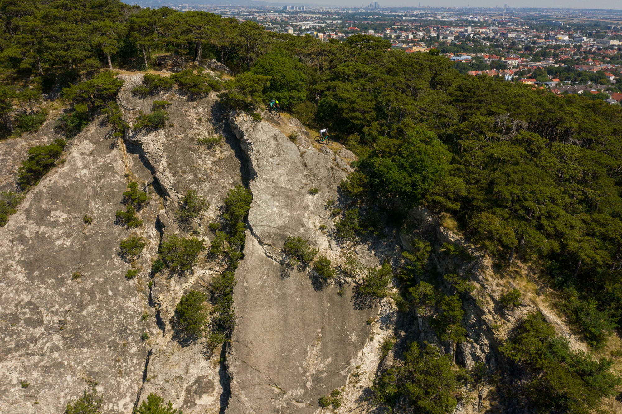 Dominik Raab und Alban Aubert fahren einen schönen Trail entlang einer Felskante und im Hintergrund sieht man die Stadt Wien